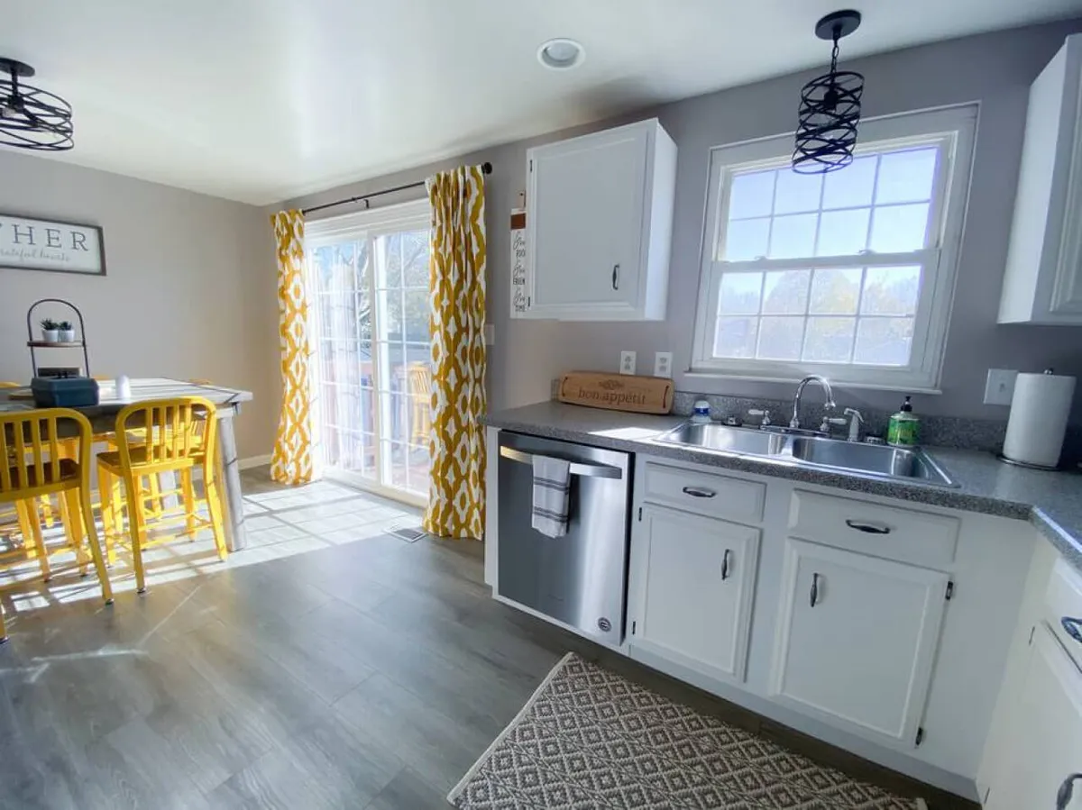 A dining nook featuring cheerful yellow chairs around a dining table, with a view of the kitchen sink and a sunlit window. The scene is ready for family meals or social gatherings, bright and welcoming.