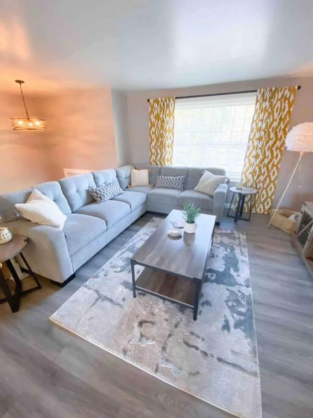 A cozy interior scene with a sectional sofa, coffee table, decorative rug, and curtains. The setup is designed for comfort and socializing, with an inviting ambiance that encourages movie nights or intimate conversations.