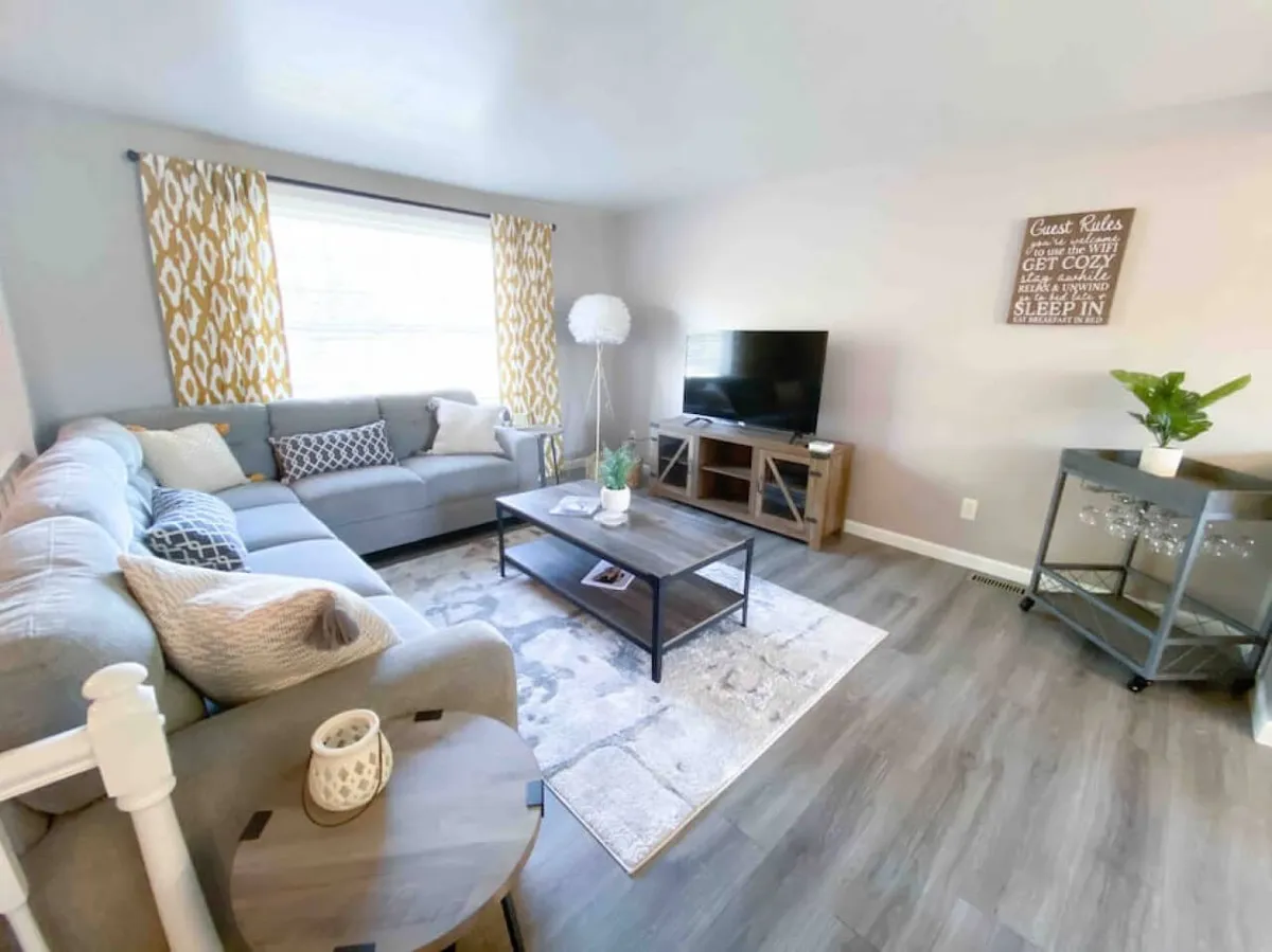 The image showcases a cozy living room with a plush sofa, stylish coffee table, TV, and soft, inviting curtains, creating a warm and welcoming atmosphere. The space is designed for relaxation, group gatherings, and quiet moments, perfect for families or friends to unwind together.
