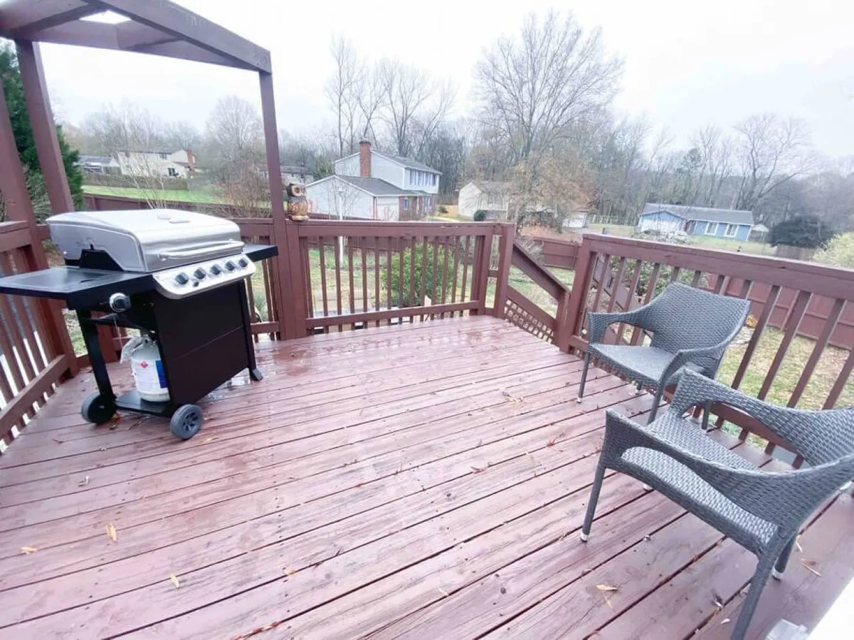 This inviting exterior shot showcases a deck with a Charbroil grill, comfortable chairs, and a relaxed outdoor dining setup. The scene suggests a space ideal for barbecuing and enjoying meals al fresco, with clear sightlines to the surrounding yard and garden.