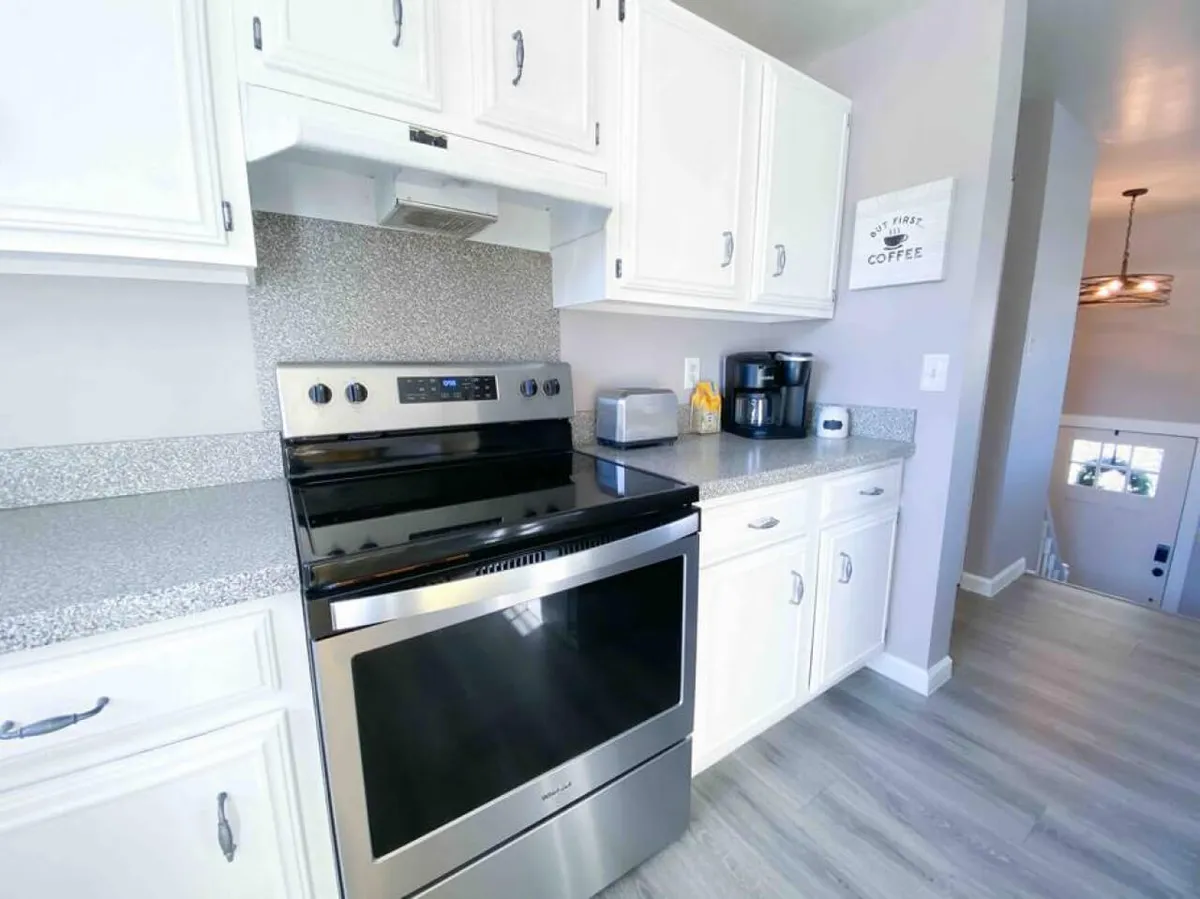 Close-up of a kitchen corner with a stainless steel stove, coffee maker, granite countertop, and white cabinetry. The space feels cozy and welcoming, perfect for both morning coffee rituals and meal preparation.